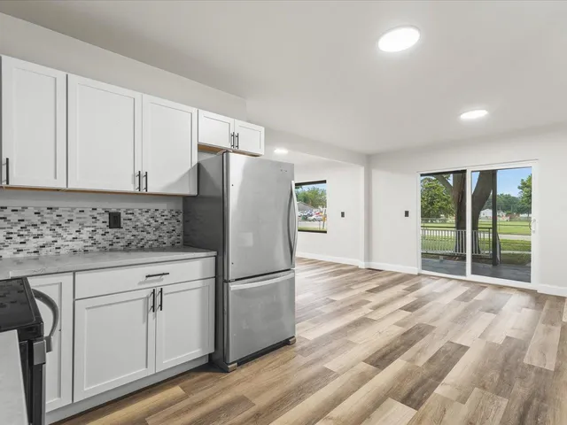 a kitchen with granite countertop a refrigerator a sink and white cabinets
