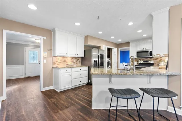 a kitchen with stainless steel appliances granite countertop a stove top oven a sink dishwasher and a refrigerator with wooden floor