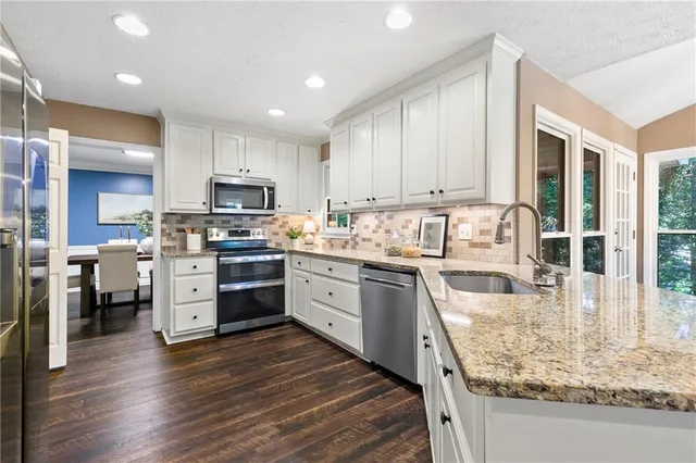 a kitchen with stainless steel appliances granite countertop a stove top oven a sink dishwasher and a refrigerator with wooden floor