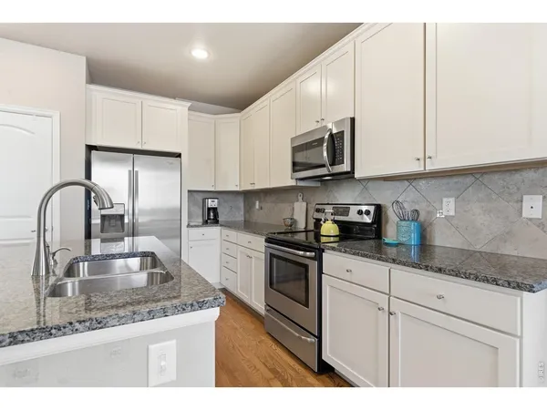 a kitchen with stainless steel appliances granite countertop a sink a stove and white cabinets