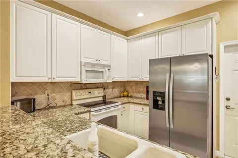 a kitchen with stainless steel appliances granite countertop a refrigerator a sink a stove and white cabinets