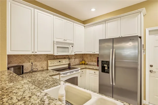 a kitchen with stainless steel appliances granite countertop a refrigerator a sink a stove and white cabinets