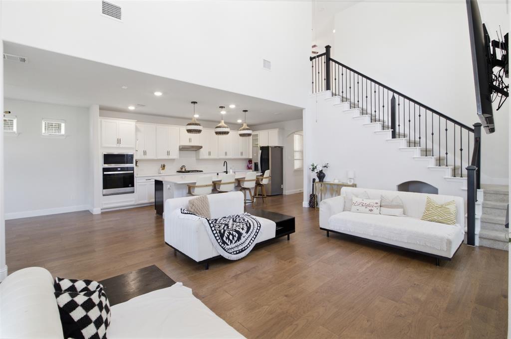 7416 Sequoia Rdg Road Little Elm, TX 76227 - Photo 16 of 37 Open-concept living space with wood-finish flooring, a two-story ceiling, and a prominent staircase featuring black iron balusters