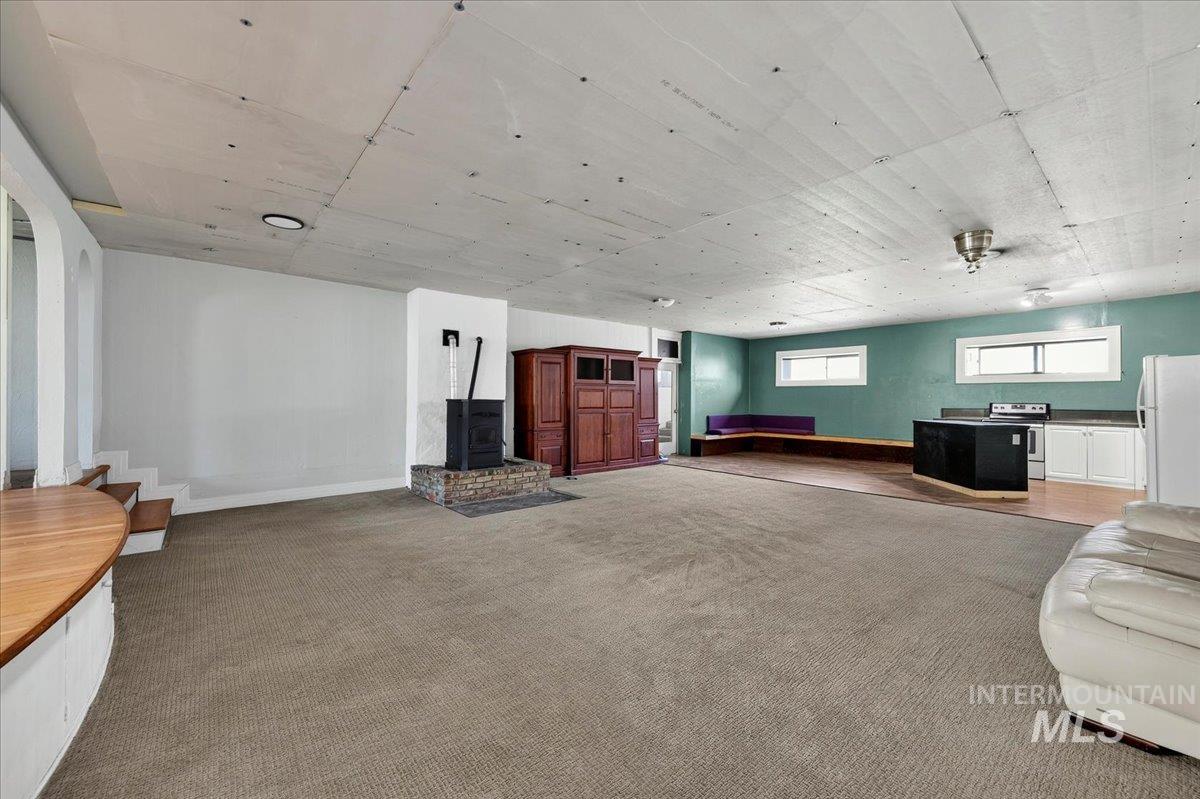 2160 South Five Mile Road Boise, ID 83709 - Photo 31 of 41 Expansive open area featuring carpeted flooring, a wood-burning stove on a stone hearth, and a partial kitchen area