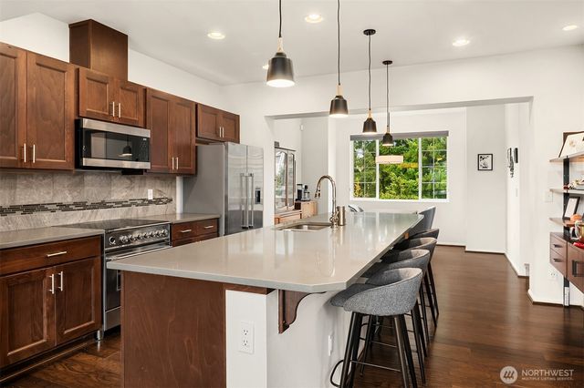 a kitchen with stainless steel appliances granite countertop a stove a refrigerator a kitchen island a sink cabinets and wooden floor