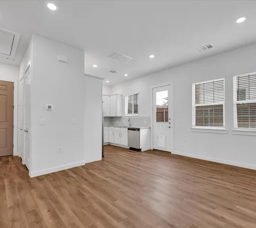 a view of an empty room with wooden floor and kitchen