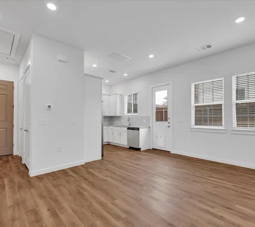a view of an empty room with wooden floor and kitchen