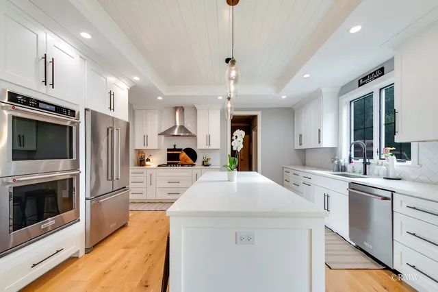 a large kitchen with stainless steel appliances kitchen island a stove a sink a refrigerator white cabinets and wooden floor