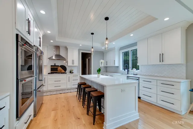 a kitchen with stainless steel appliances kitchen island granite countertop a stove top oven a sink a dining table and chairs with wooden floor