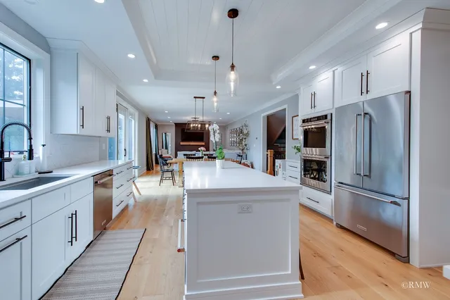 a kitchen with granite countertop a refrigerator oven a sink dishwasher and white cabinets with wooden floor
