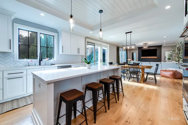 a kitchen with kitchen island a dining table chairs sink and white cabinets