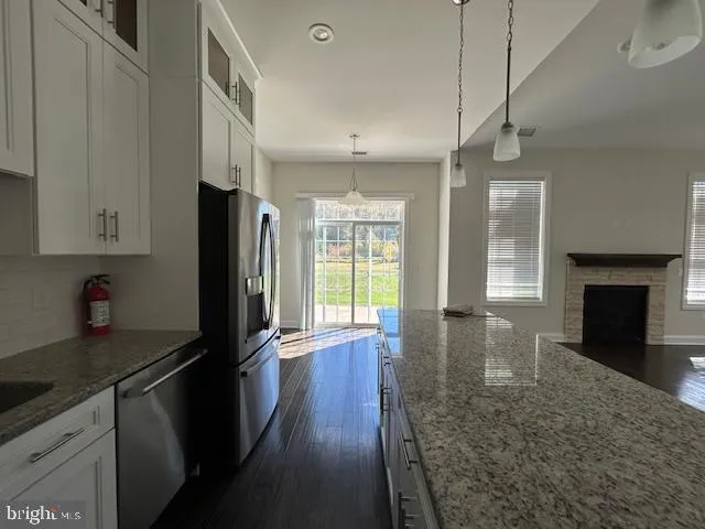 a kitchen with granite countertop stainless steel appliances a stove a refrigerator a sink and a fireplace with wooden floor