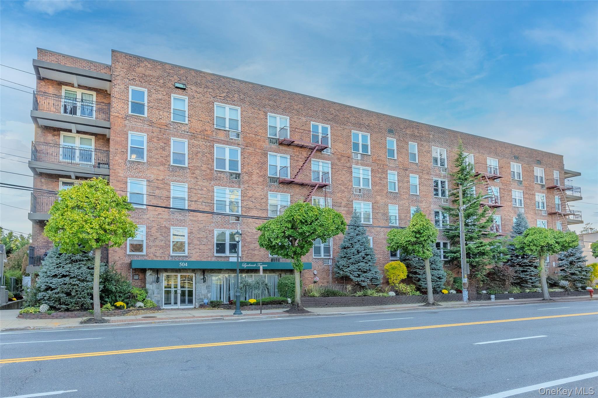 504 Merrick Road, Unit 4E Lynbrook, NY 11563 - Photo 2 of 19 a front view of a building with garden and parking