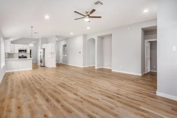 a view of an empty room and kitchen view with wooden floor