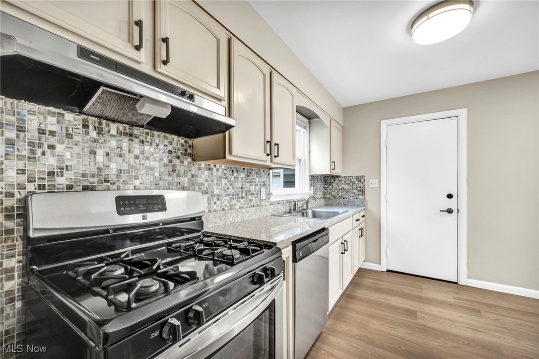 1682 Overbrook Road Lyndhurst, OH 44124 - Photo 6 of 33 Kitchen with under cabinet range hood, appliances with stainless steel finishes, decorative backsplash, light countertops, and light wood-style floors