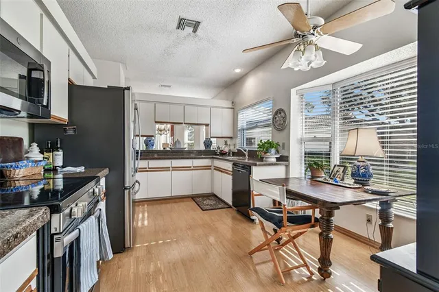 a kitchen with stainless steel appliances kitchen island granite countertop a refrigerator a stove a sink a dining table and chairs with wooden floor