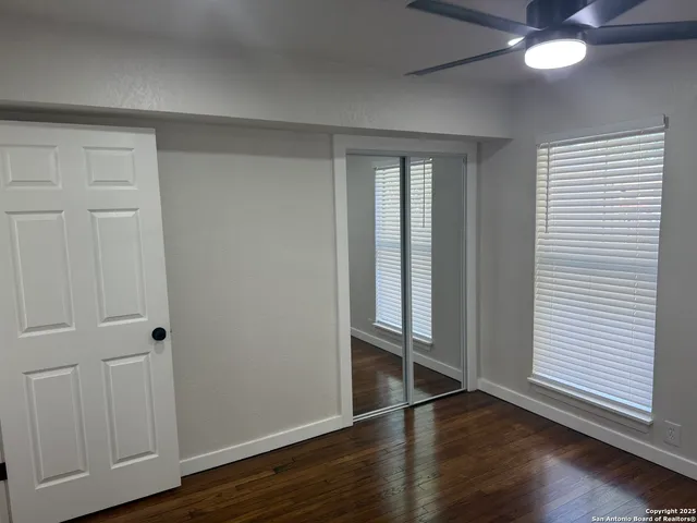 an empty room with wooden floor fan and windows