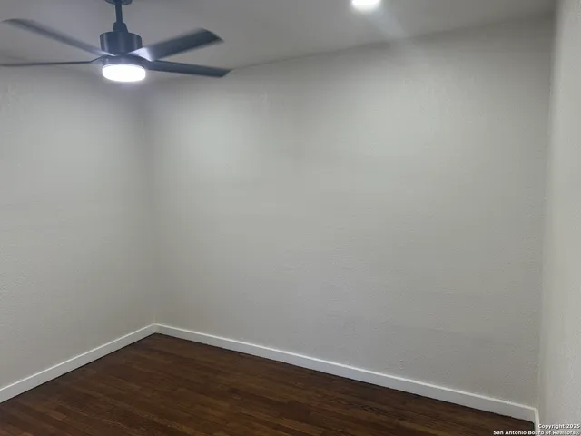 an empty room with wooden floor cabinet and a ceiling fan