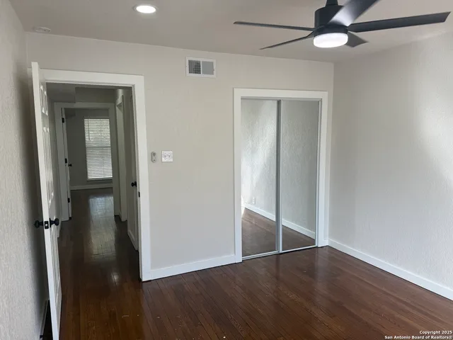 an empty room with wooden floor fan and windows