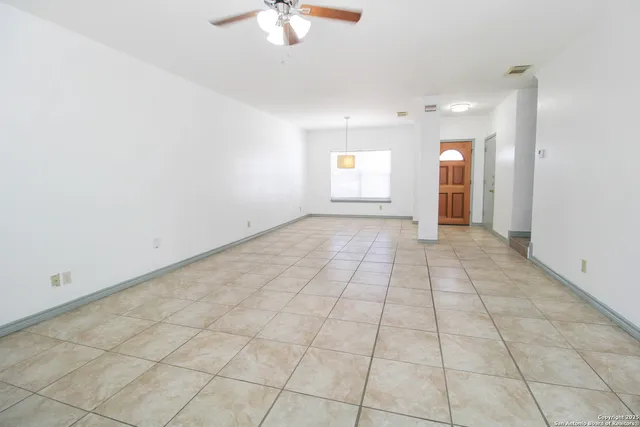 an empty room with white walls and chandelier fan