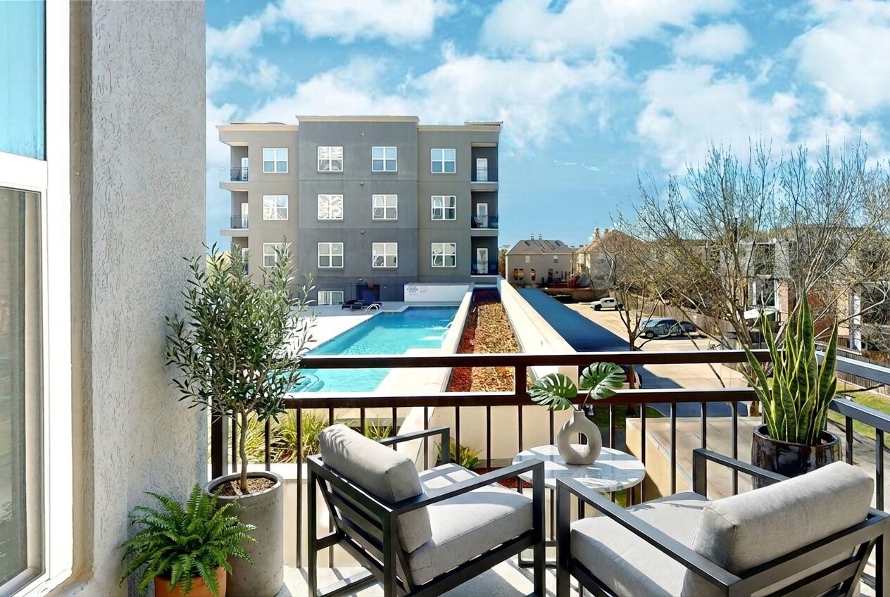 1010 Rosine Street, Unit 29 Houston, TX 77019 - Photo 1 of 16 This photo showcases a bright and inviting balcony with comfortable seating and plants, overlooking a communal pool and a modern apartment building. Ideal for relaxation and enjoying the view. (Virtual Staging)