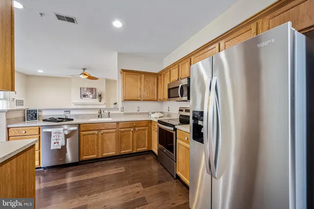 a kitchen with stainless steel appliances granite countertop a refrigerator a sink dishwasher a stove top oven a refrigerator and white cabinets with wooden floor
