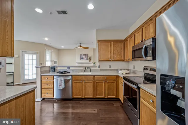 a kitchen with stainless steel appliances granite countertop a stove top oven a sink dishwasher a refrigerator and a cabinets with wooden floor