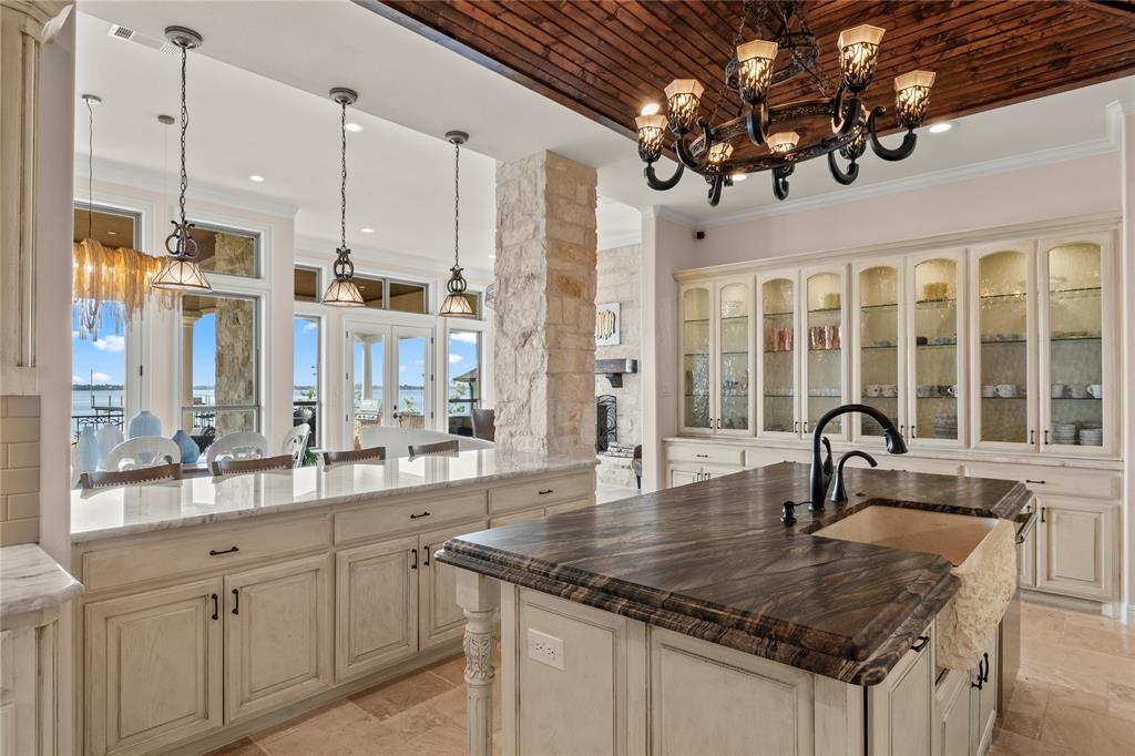 204 Pinnacle Club Place Mabank, TX 75156 - Photo 12 of 40 Cook with a view—panoramic water scenes framed by stone accents and a warm wood ceiling. Custom cabinetry with aesthetic appealing glass fronts for decorative display and amazing amount of storage.