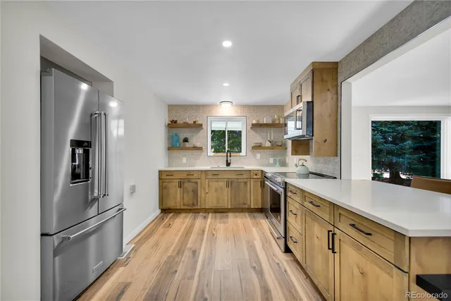 a large kitchen with stainless steel appliances a refrigerator a sink dishwasher a stove and white cabinets with wooden floor