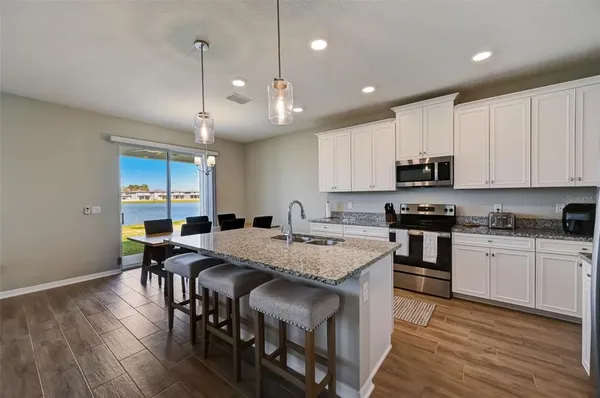 a kitchen with stainless steel appliances granite countertop a stove top oven a refrigerator a sink and a dining table with wooden floor