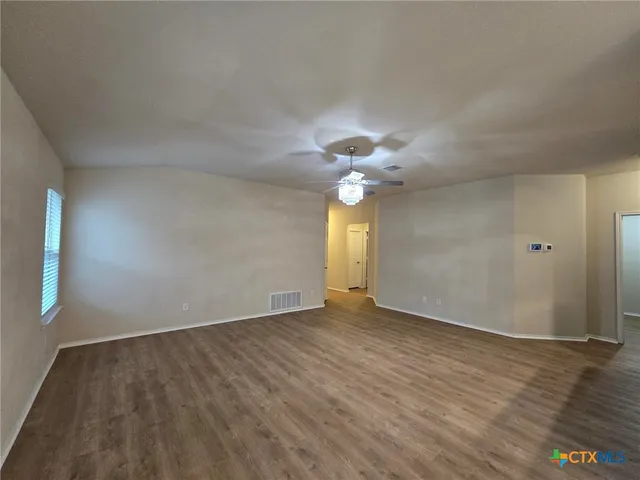 an empty room with wooden floor chandelier fan and windows