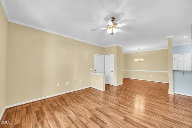 a view of an empty room with wooden floor and a chandelier fan