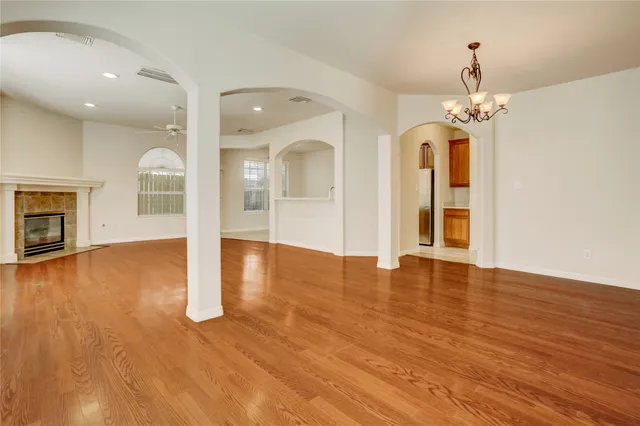 an empty room with wooden floor chandelier and windows