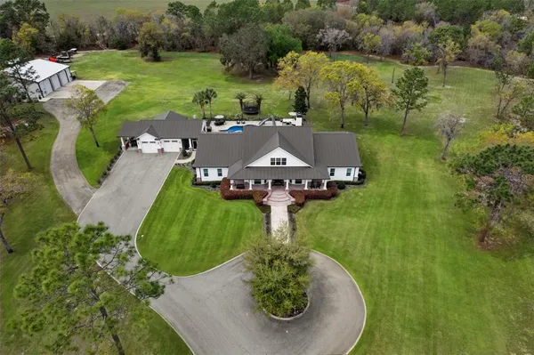 an aerial view of a house with outdoor space tennis court and trees all around
