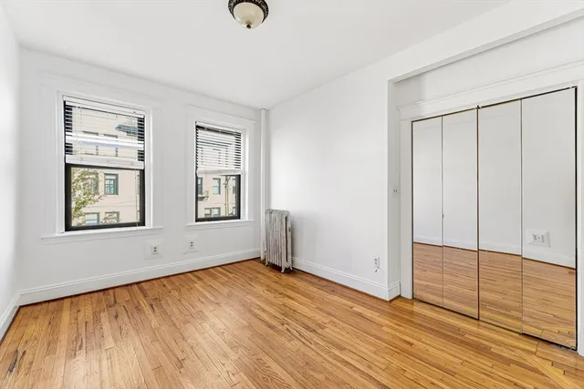 an empty room with wooden floor closet and windows