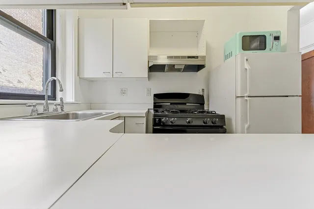 a white kitchen with sink a refrigerator and white cabinets