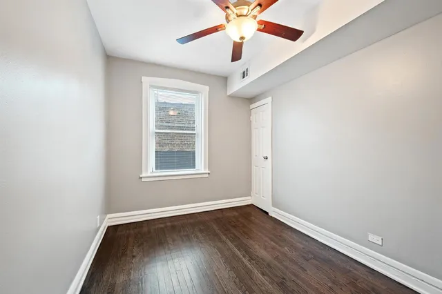 an empty room with wooden floor chandelier fan and windows