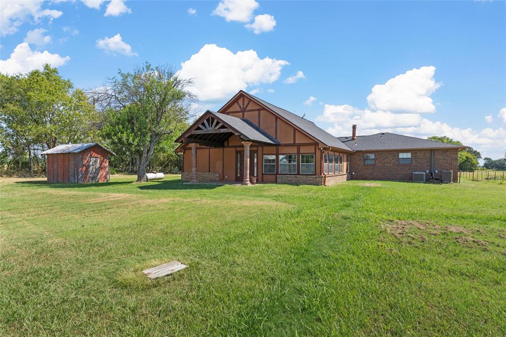 3433 West Tours Road West, TX 76691 - Photo 34 of 40 Back of property with a lawn, a storage shed, brick siding, and a patio area