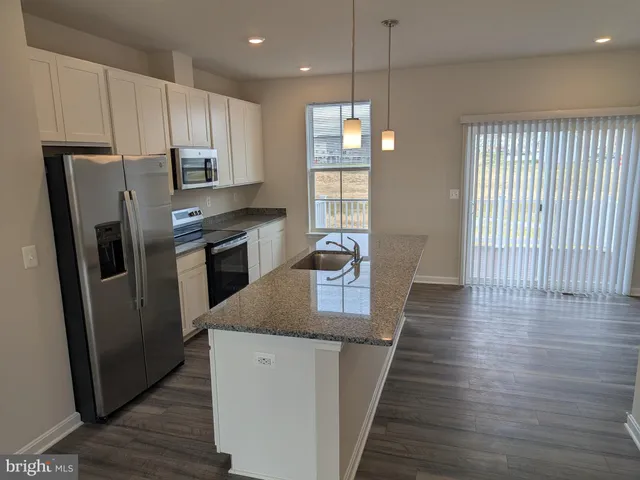 a kitchen with stainless steel appliances granite countertop a refrigerator a sink dishwasher a stove and white countertops with wooden floor