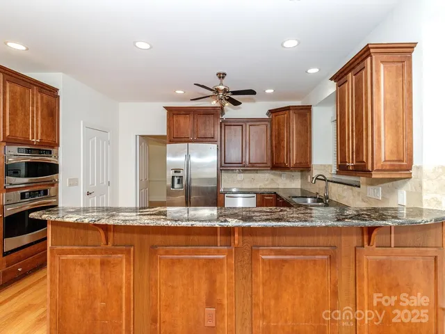 a kitchen with stainless steel appliances granite countertop a sink a stove a refrigerator a center island and cabinets
