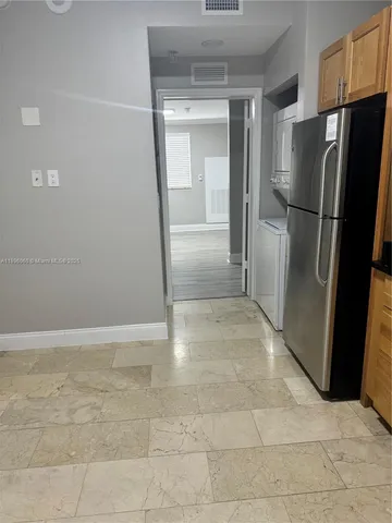 a view of a refrigerator in kitchen and an empty room