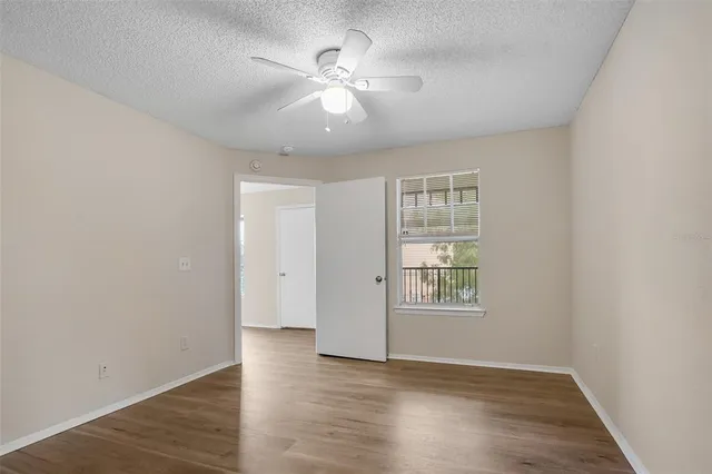 an empty room with wooden floor chandelier fan and windows