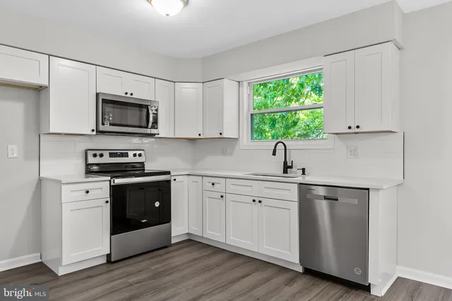 a kitchen with stainless steel appliances granite countertop white cabinets a sink a stove a microwave and wooden floors