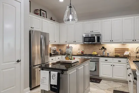 a kitchen with stainless steel appliances granite countertop a refrigerator stove a sink and white cabinets