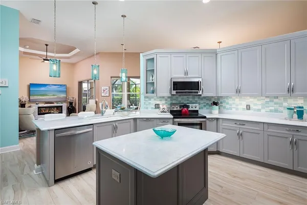 a kitchen with stainless steel appliances granite countertop a stove a sink a microwave a refrigerator and white cabinets with wooden floor