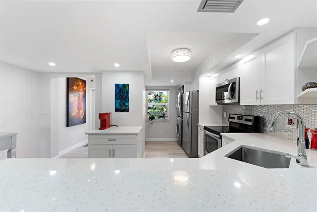 a kitchen with stainless steel appliances a microwave a sink a stove a refrigerator cabinets and living room view