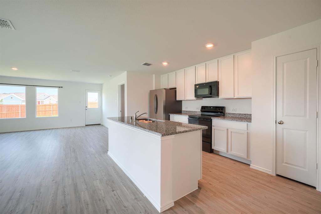 5916 Crystal Water Way Princeton, TX 75407 - Photo 5 of 28 a kitchen with sink a microwave oven a refrigerator and white cabinets with wooden floor