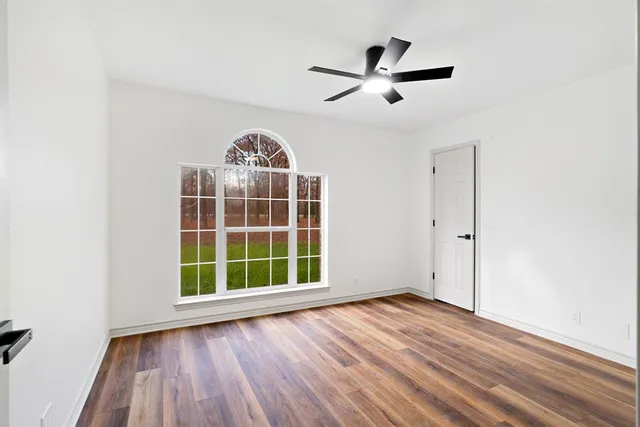 an empty room with wooden floor a ceiling fan and windows