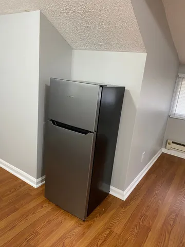a view of a refrigerator in kitchen and an empty room with wooden floor