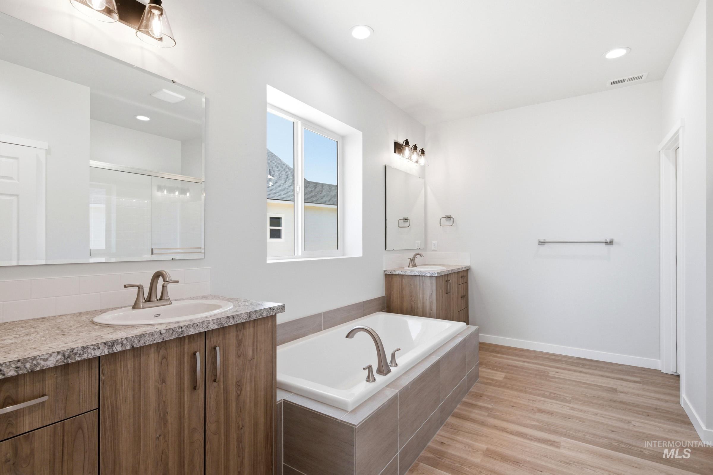 13649 Inman Court Caldwell, ID 83607 - Photo 21 of 22 Bathroom featuring a built-in tub with tile surround, dual wood-finish vanities with light-colored countertops, and wood-finish flooring